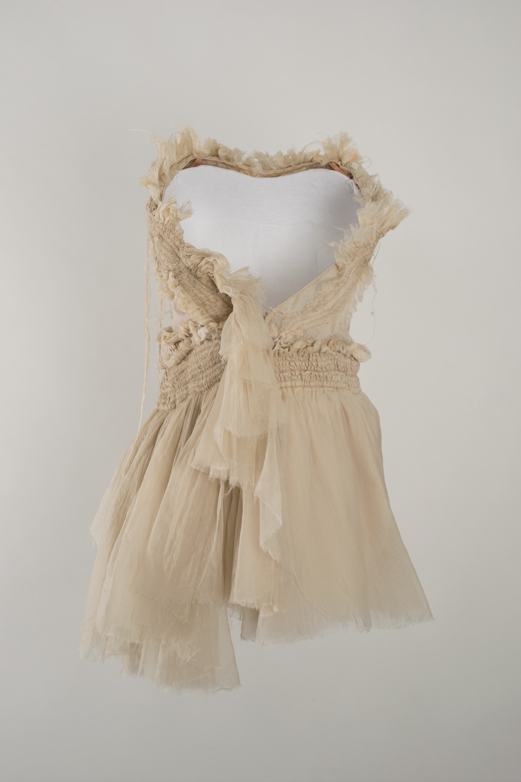 A dance costume designed by Akira Isogawa that is supported by one of the 'invisible' white moulded forms. The dress is made from off-white fabric, with a short skirt, wide v-neck and elasticated waist. The edges of the fabric are left deliberately frayed.